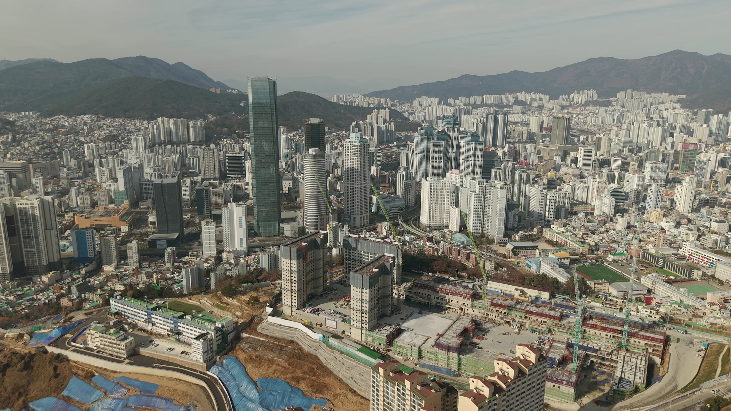 국제금융센터와 아파트들을 뒤로 하고, 타워크레인 아래 새 건물이 올라가는 문현동 언덕을 드론으로 내려다본 모습