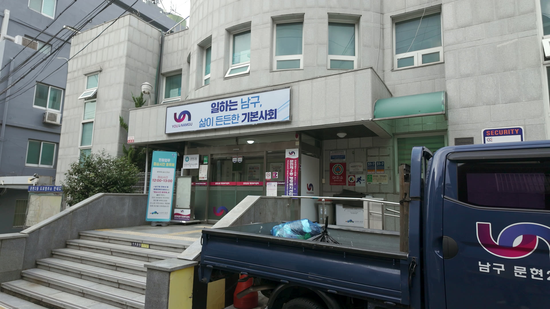 ‘일하는 남구’ 현수막이 걸린 문현2동 행정복지센터 입구 계단과, 그 앞에 선 ‘남구 문현2동’ 글씨가 적힌 파란 트럭
